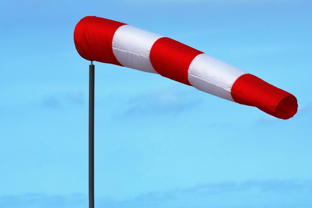 Red and white windsock indicating wind direction and speed against a clear blue sky.